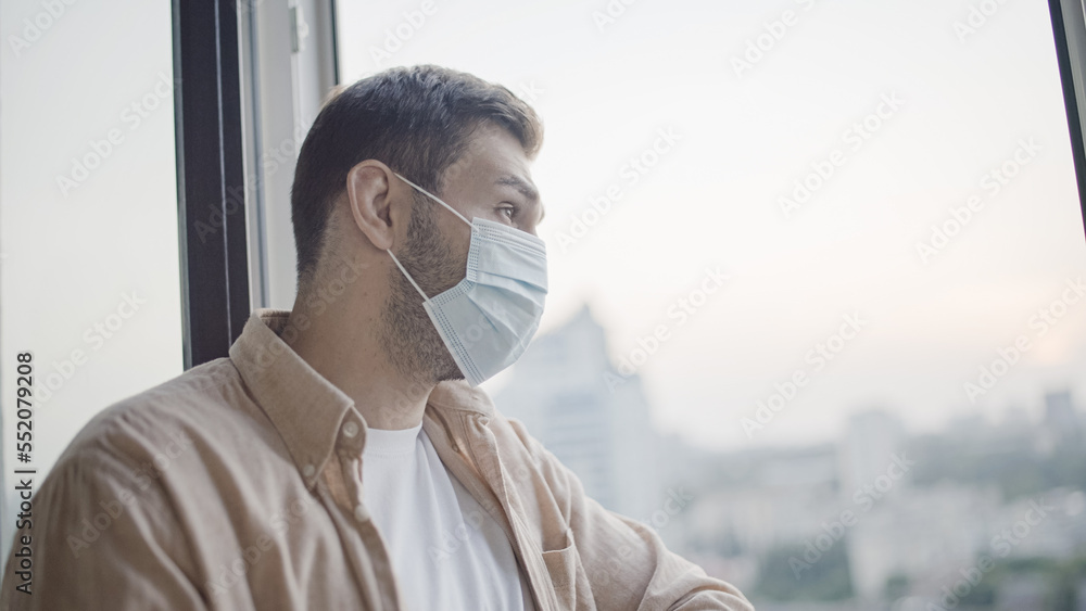 Middle-aged man in protective face mask looking out window, pandemic safety Middle-aged man in protective face mask looking out window, pandemic safety