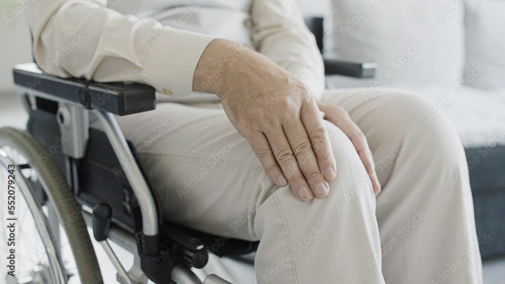 Close-up of man in wheelchair rubbing injured knee, rehabilitation after injury, arthritis Close-up of man in wheelchair rubbing injured knee, rehabilitation after injury, arthritis