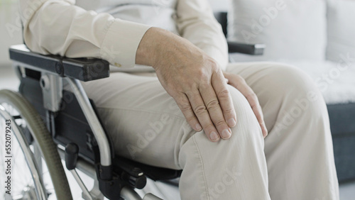 Close-up of man in wheelchair rubbing injured knee  rehabilitation after injury  arthritis