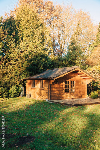 Small wooden house in a beautiful garden with lots of sun. Garden in summer or spring. Wooden garden shed. Secluded little cottage in the woods © Marianna