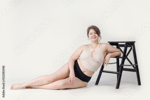 A large woman in underwear lying on the floor on a light background. Plump girl plus size, positive attitude to the body.