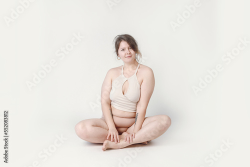 A plump woman with a hairstyle, smiling at the camera, sitting in the studio in her underwear. A bodypositive large-sized woman who feels comfortable in her natural body.