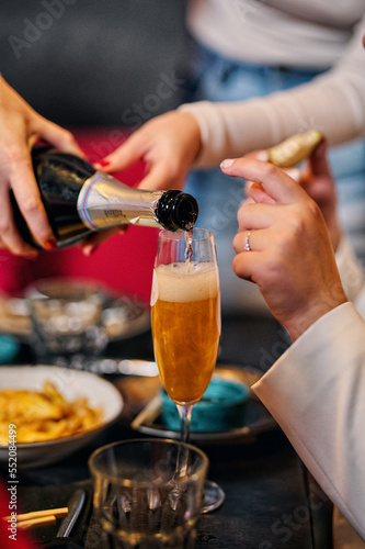 The waiter pours champagne into glasses on the table at the Bachelorette. Women's hands. Open a bottle of alcohol. Holiday