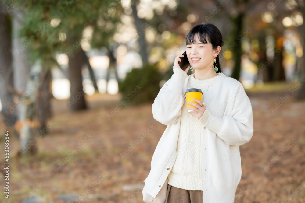 Fototapeta premium ホットドリンクを飲みながら電話する女性