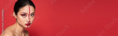 young asian woman with creative visage and ear cuff looking at camera isolated on red, banner.