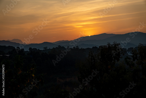 orangener goldener Sonnenuntergang in Chiang Rai, Norden von Thailand mit Bergen im Hintergrund, hinter welche die Sonne verschwindet