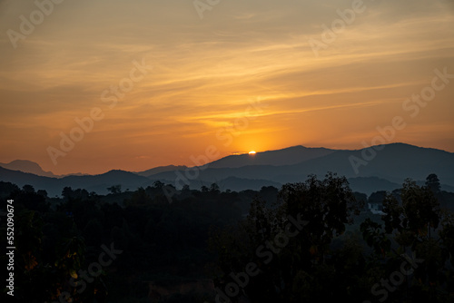 orangener goldener Sonnenuntergang in Chiang Rai, Norden von Thailand mit Bergen im Hintergrund, hinter welche die Sonne verschwindet