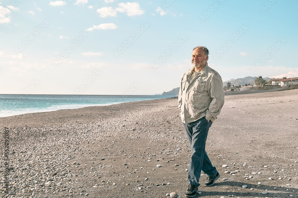 Happy middle-aged bearded man walking along deserted winter beach. Concept of leisure activities, wellness, freedom, tourism, healthy lifestyle and nature.