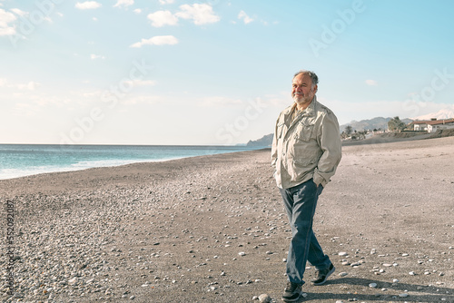 Happy middle-aged bearded man walking along deserted winter beach. Concept of leisure activities, wellness, freedom, tourism, healthy lifestyle and nature.