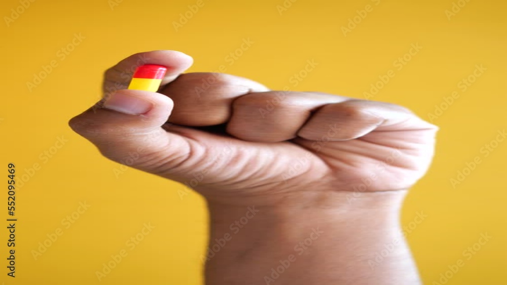 Close up of man hand holding a capsule against yellow background Close up of man hand holding a capsule against yellow background