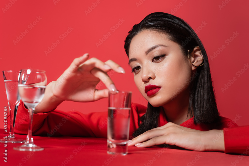 young asian woman with makeup touching glass with pure water isolated on red. young asian woman with makeup touching glass with pure water isolated on red.