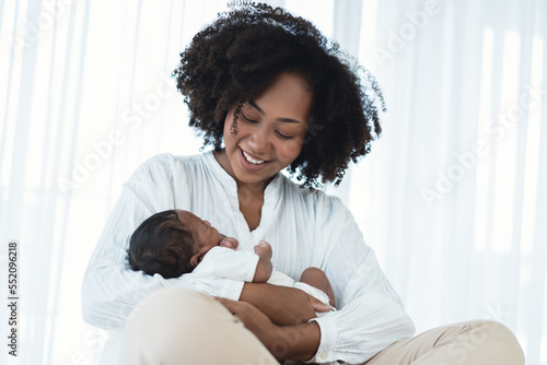 Smiling African American mother holding newborn baby in her arms. Loving Black mom hug embrace small baby child, relax enjoy tender family moment in bedroom. Beautiful family, Mother's day concept.