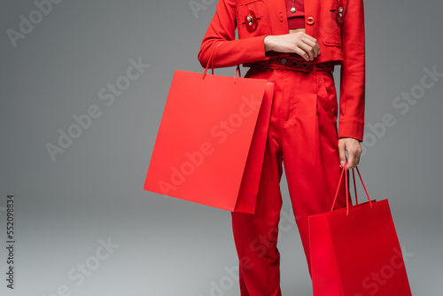 partial view of woman in red suit standing with shopping bags on grey background.