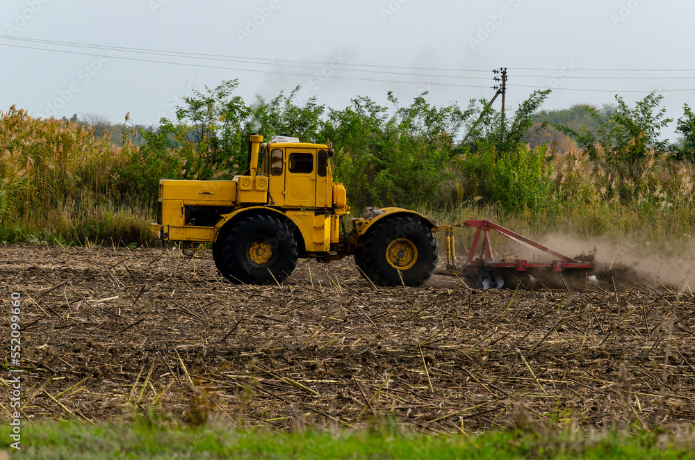 The tractor prepares the land with the help of a cultivator for pre-sowing work, on rice checks. Cultivated field Agronomy farming concept The tractor prepares the land with the help of a cultivator for pre-sowing work, on rice checks. Cultivated field Agronomy farming concept