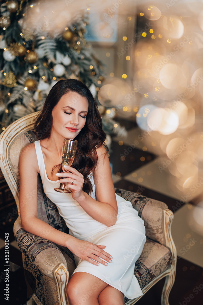 Stylish beautiful woman in a New Year's dress sits in a chic restaurant. A young slender girl in an evening dress stands in a New Year's studio. Happy girl celebrates christmas and drinks champagne.