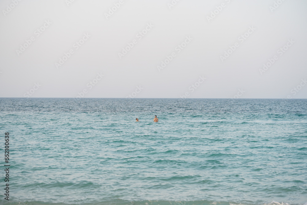 Two people swim in the middle of the beach, very far away.