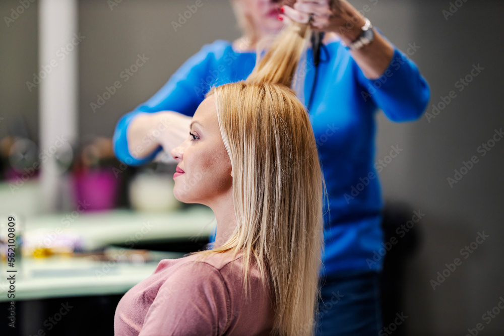 Fototapeta premium A happy customer is sitting in hair salon while hair stylist is styling her hair.