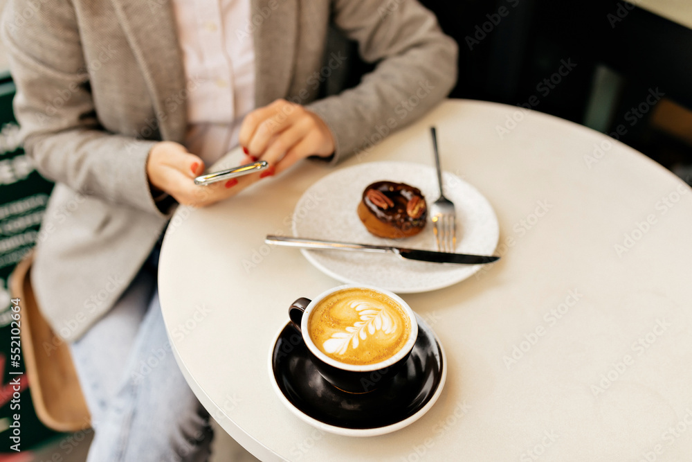 Top view of woman hands is holding smartphone and having brunch. Young woman sitting on table with coffee and dessert