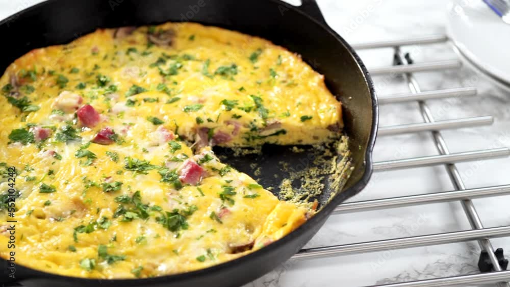 Slicing freshly baked spinach and ham frittata in cast iron skillet. Slicing freshly baked spinach and ham frittata in cast iron skillet.