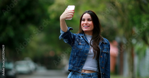 Young woman holding smartphone taking selfie outdoors