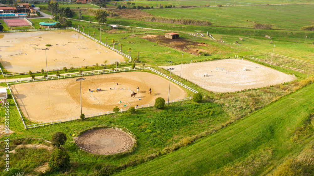 Aerial view of three horsemen. A riding field with fence and obstacles to train horses. In this sports facility, tournaments and horse racing courses are organized. The sports center is in the nature.