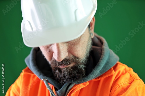 Close-up of man with beard wearing worker uniform and hardhat. Helmet visor covering the eyes.