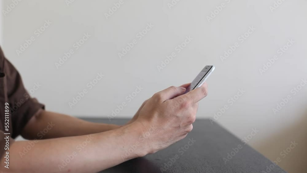 スマートフォンを操作する男性の手元。テーブルの上に手をおいて白いスマートフォンを操作している。スワイプやタップなどの操作。 スマートフォンを操作する男性の手元。テーブルの上に手をおいて白いスマートフォンを操作している。スワイプやタップなどの操作。