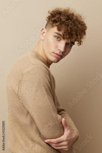 a handsome, attractive man in stylish clothes stands on a beige background sideways to the camera and poses relaxed