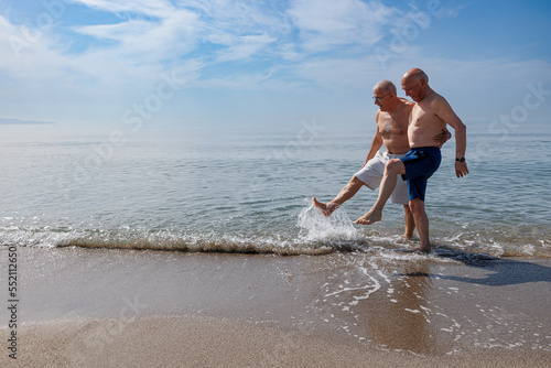 coppia di anziani al mare giocano sula riva schizzando e calciando l''acqua photo