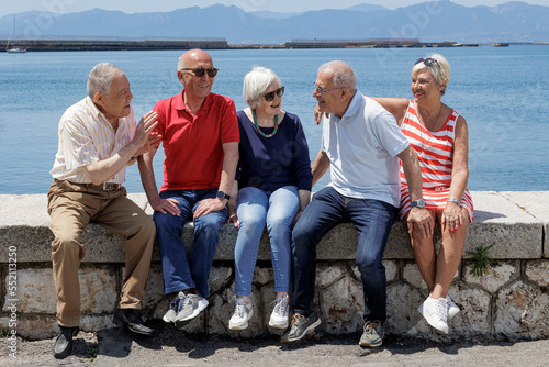 gruppo di anziani amici seduti nel muretto di un porto di mare, si rilassano chiacchierando felici. photo