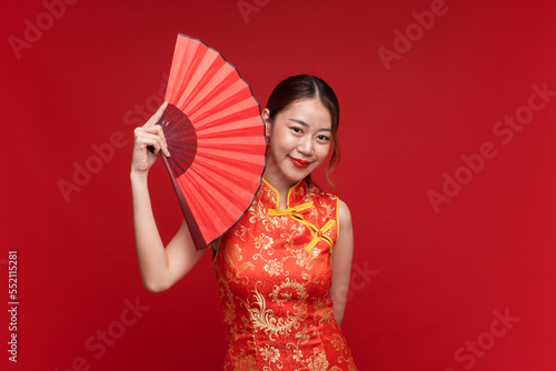 Young asian woman wearing qipao cheongsam dress with Chinese folding fan on red background for Chinese new year festival © Nattakorn