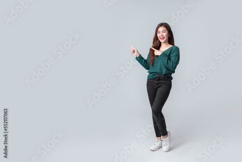 Full length Asian woman in casual green sweater pointing to empty space on isolated grey background. Happy anniversary or new year festival concept. photo