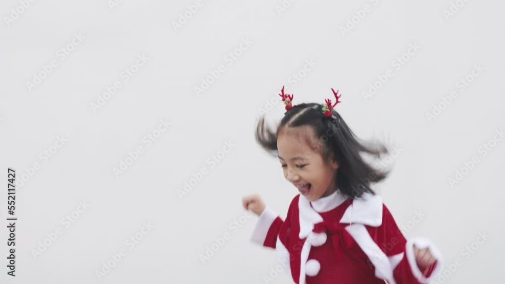 Adorable asian girl kid who is costuming red sweater for Christmas celebration is dancing, laughing and smiling on white background shows concept of happiness moment with cheerful and fun emotion. Adorable asian girl kid who is costuming red sweater for Christmas celebration is dancing, laughing and smiling on white background shows concept of happiness moment with cheerful and fun emotion.