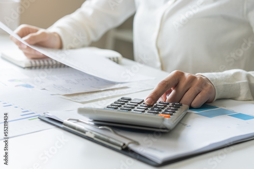 Account finance, analysis asian young business woman hand use calculator for calculate budget, cost and income of company from reports paperwork, plan spend money expenses, working on desk at home.