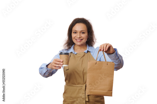 Grocery store employees. Small business and coffee shops concept. Friendly woman barista holding takeaway drink in disposable cup and paper bag, smiling as serving order to clients, white background