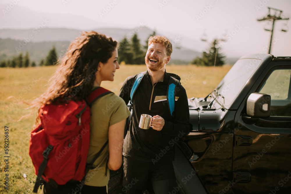 Smiling couple preparing hiking adventure with backpacks by terrain vehicle
