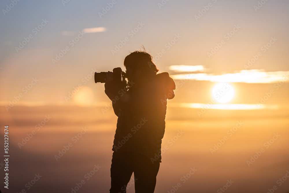 girl taking pictures at sunset with orange sky in winter clothes in the mountains