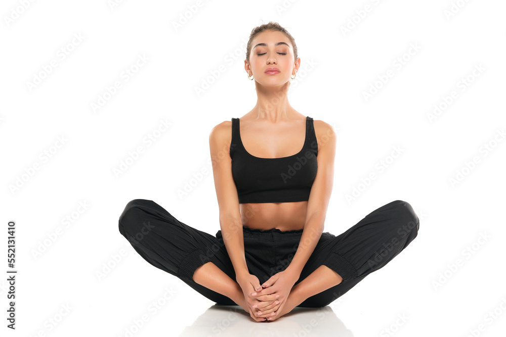 young woman in sport clothes sitting on the floor in lotus position on white background