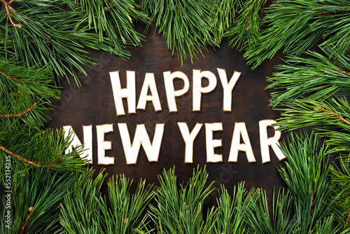 Greeting card for the New Year, top view. Fir branches with long needles against a dark wooden surface. The inscription Happy New Year in the center