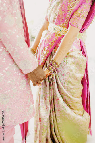 Beautiful couple of newlyweds holding hands together, dressed in light pink colors Hindu costumes