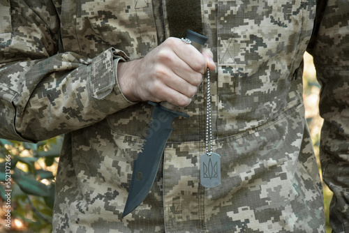 A Ukrainian military man is holding a knife and a military token with a trident.