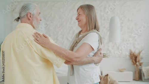 Happy funny elderly old couple dancing in the living room. A lovely husband holds the hand of his beloved wife people enjoy life together and feel happy. Modern apartments
