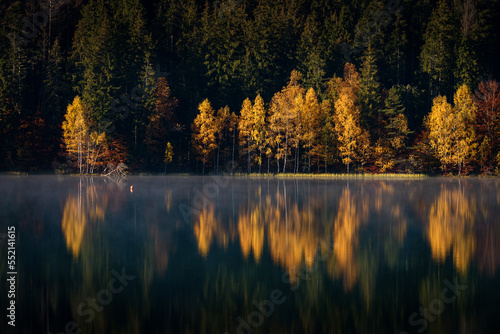 Beautiful colourful landscape in autumn season with rays of light in forest and lake reflection. Romania