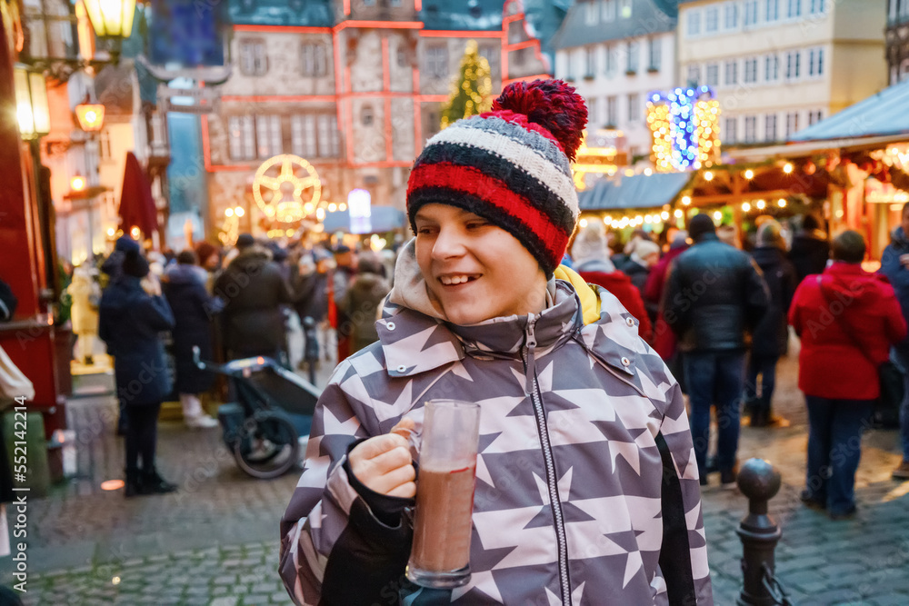 Little cute kid boy drinking hot children punch or chocolate on German Christmas market. Happy child on traditional family market in Germany, Laughing boy in colorful winter clothes