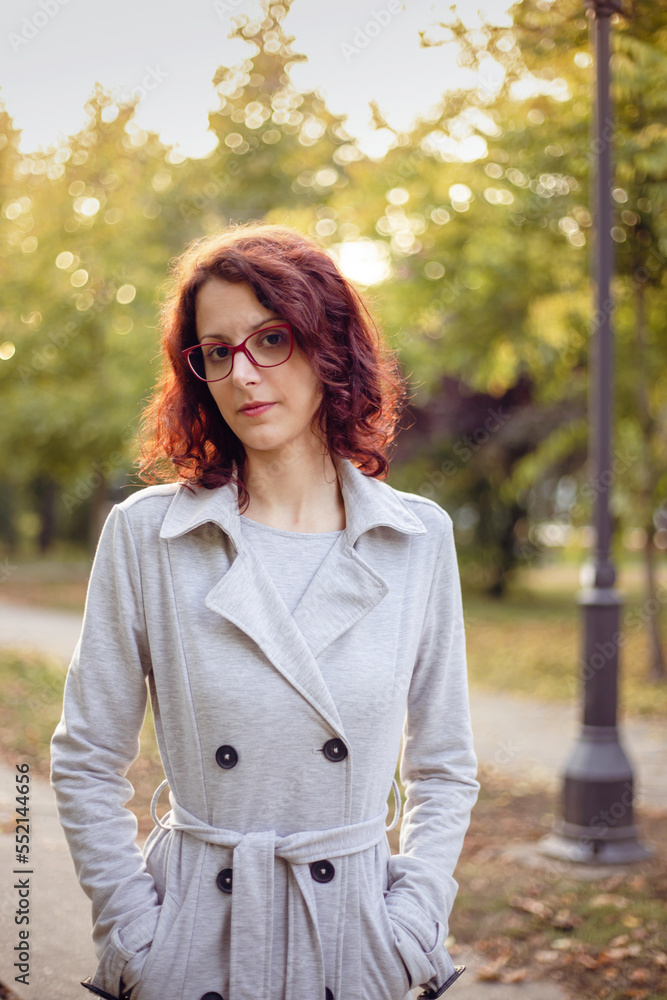 Beautiful elegant woman standing in a park in autumn. Portrait of a young beautiful girl in a grey coat with glasses. Beautiful elegant woman standing in a park in autumn. Portrait of a young beautiful girl in a grey coat with glasses.