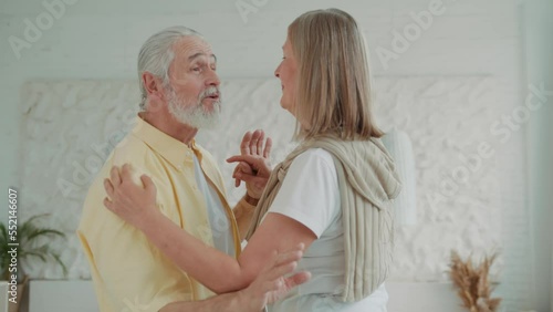 Romantic old couple dancing in the living room, the loving husband holds the hand of his beloved wife. Enjoy life together and feel happy. Modern apartments