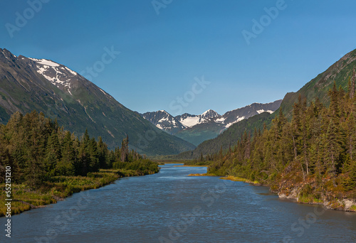 Moose Pass, Alaska, USA - July 22, 2011: Blue water Clear Creek meandering between green forests and dark mountains with snow patches under blue sky