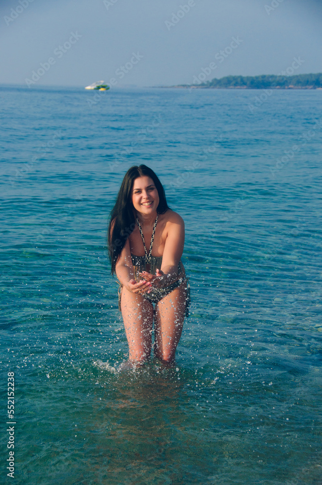 Young brunette splashing on the beach. Portrait of a positive girl at the sea in summer
