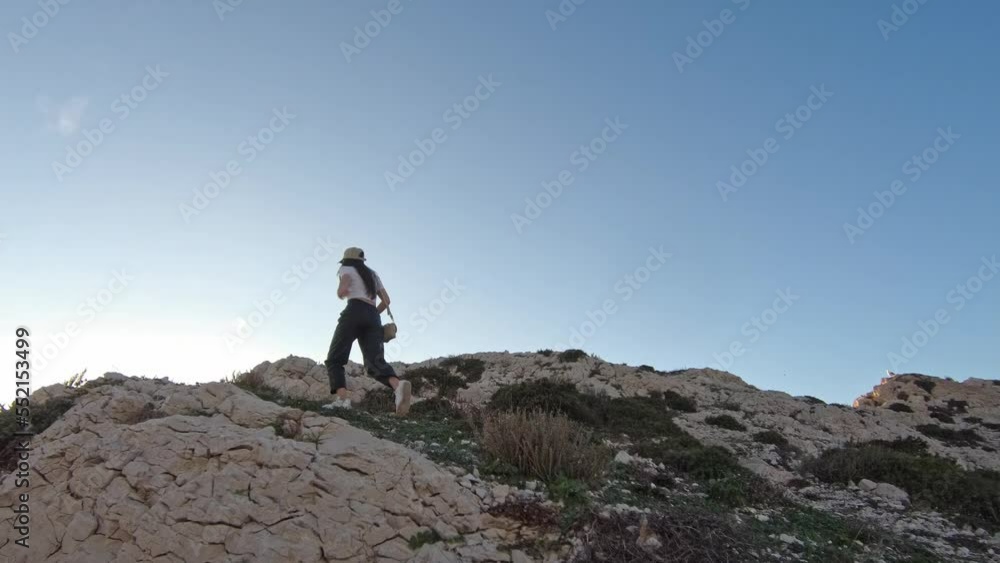 A young Caucasian girl climbs with a left-handed run up the very peak of a mountain in the afternoon on the island of Friulle in France, a side view with slow motion and tracking to the left. Journey A young Caucasian girl climbs with a left-handed run up the very peak of a mountain in the afternoon on the island of Friulle in France, a side view with slow motion and tracking to the left. Journey