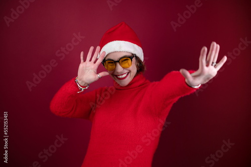 Young positive woman in christmas santa hat isolated over redl background. Happy young woman in Santa's helper hat a red background. photo